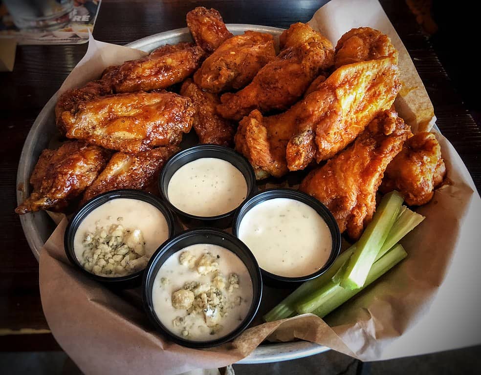 A plate of buffalo chicken wings with sides of celery, and blue cheese and ranch sauces for dipping