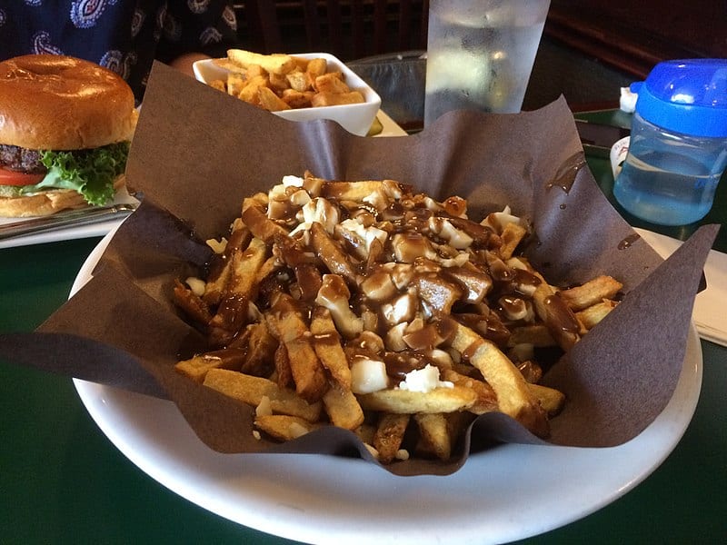 A plate of poutine (fries! gravy! cheese curds!) on a table with a hamburger, french fries, and a blue sippy cup