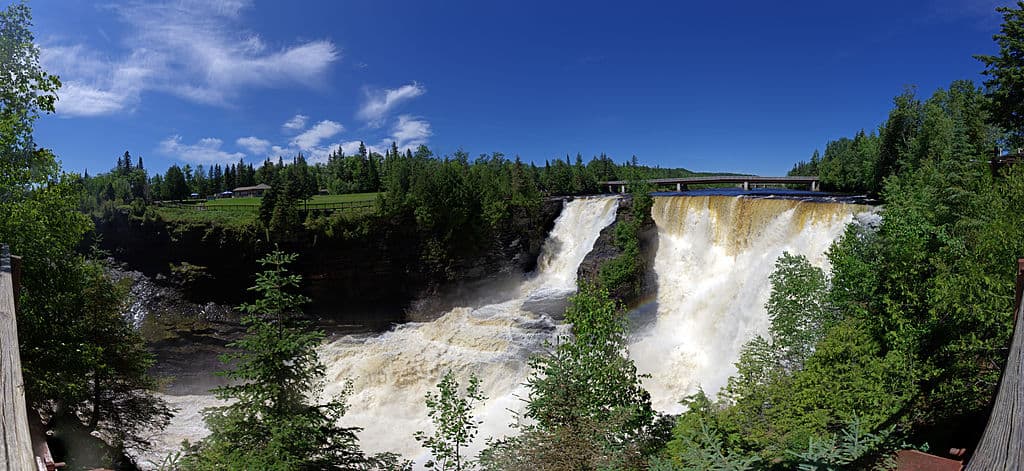 A panoramic view of a wide waterfall framed by tall spruce trees (Kakabeka Falls, Ontario)