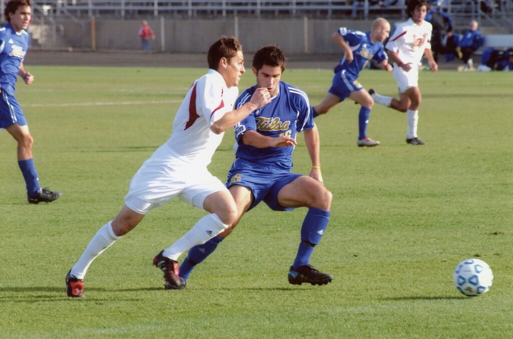 A college-level soccer game underway, with two players running for the ball mid-stride.