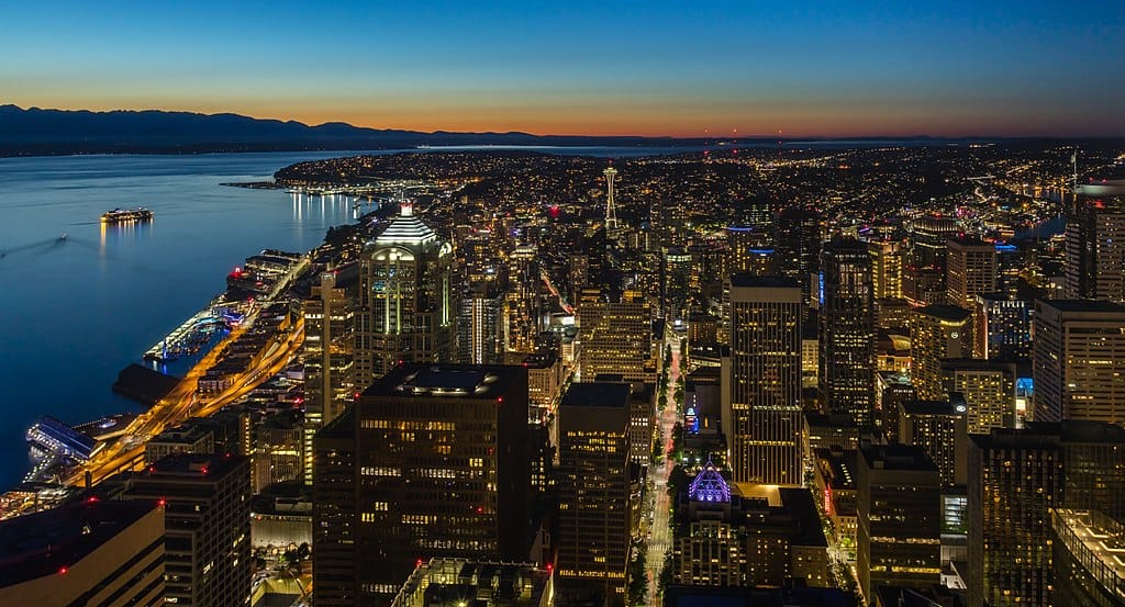 A high-vantage view of Seattle, Washington - a large coastal city at dusk with city streets and buildings lit up.