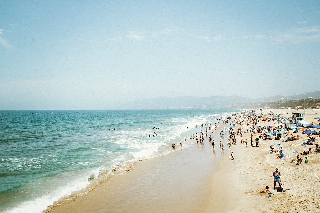 Beach landscape: gentle waves lap a long golden sand beach, filled with vacationers. The sky is clear and blue. (Santa Monica, CA)