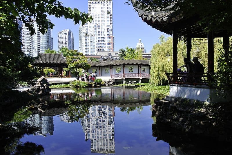 A large manmade pond is framed by traditional Chinese architecture. Modern skyscrapers tower over the classical buildings in the background.