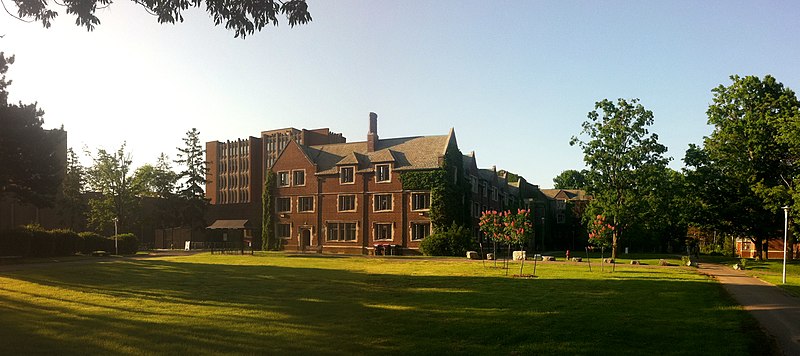 A red brick building at the back of a lush green lawn, framed by leafy green trees (Edwards Hall, McMaster University)