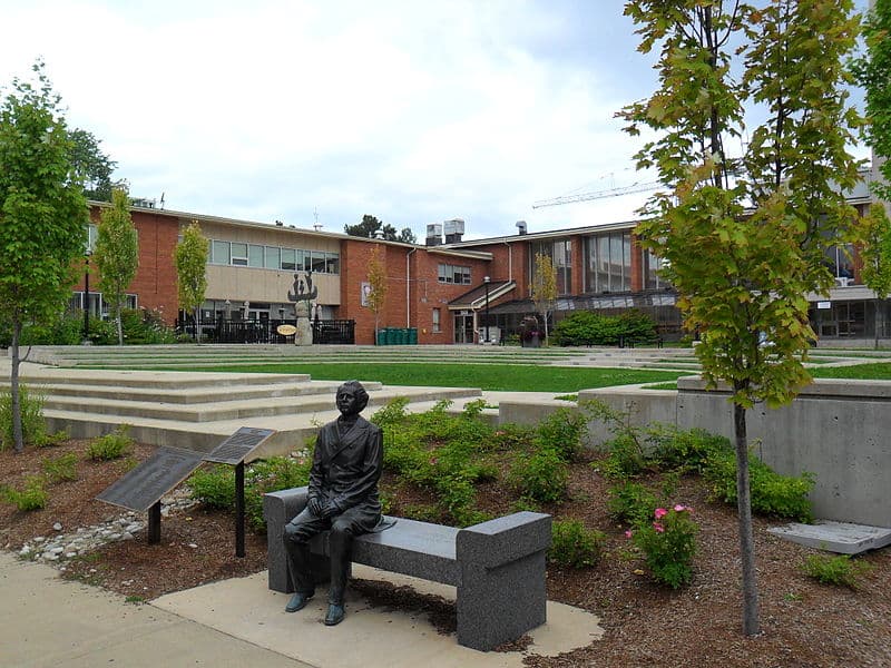 Mid-level red brick buildings frame a green lawn and a bronze statue of Wilfrid Laurier, at Wilfrid Laurier University
