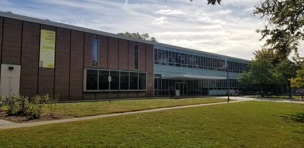 A two-storey brick building sits behind a green campus lawn at one of the Centennial College campuses.