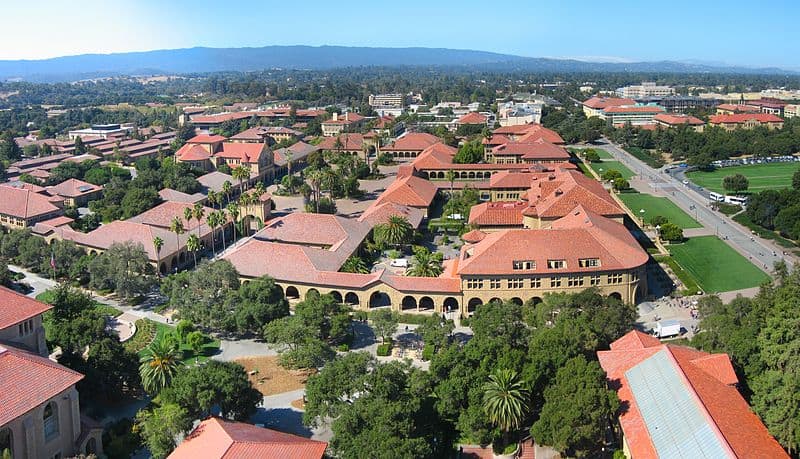 The Stanford campus from an aerial view: green deciduous trees, red-roofed buildings in the Richardsonian Romanesque style.
