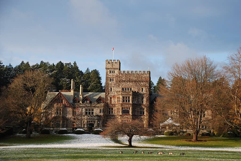 A red-brick, castle-like building rises behind deciduous trees that have dropped their leaves on a wide green lawn. It's part of Royal Roads University in BC, Canada.