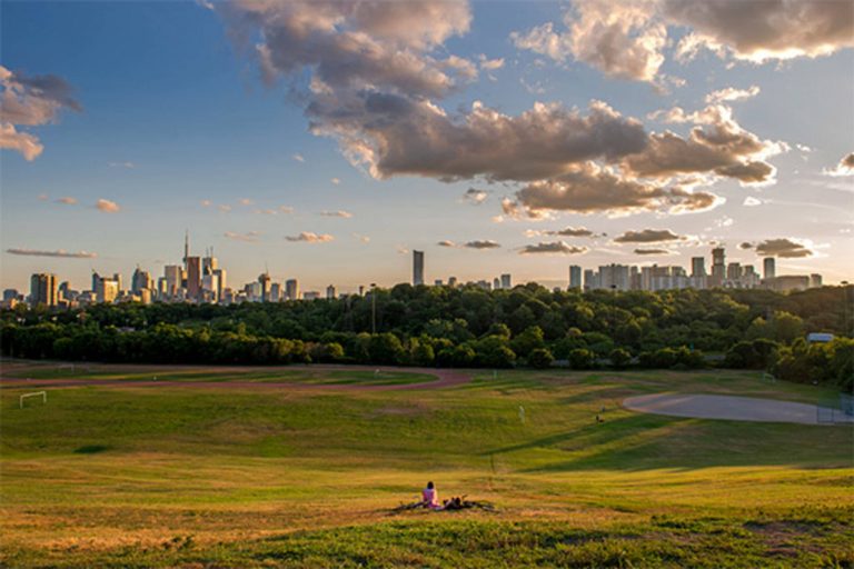 An image of green space at Riverdale Park in Toronto, with clouds in a blue sky and the sun about to set.
