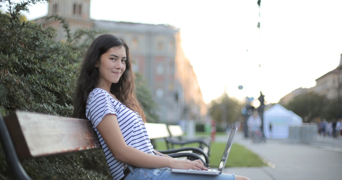 Girl working on laptop on park bench
