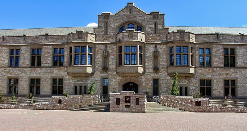 A two-storey stone building on a broad paved walk, with a bright blue sky behind. (University of Saskatchewan's Nobel Plaza)