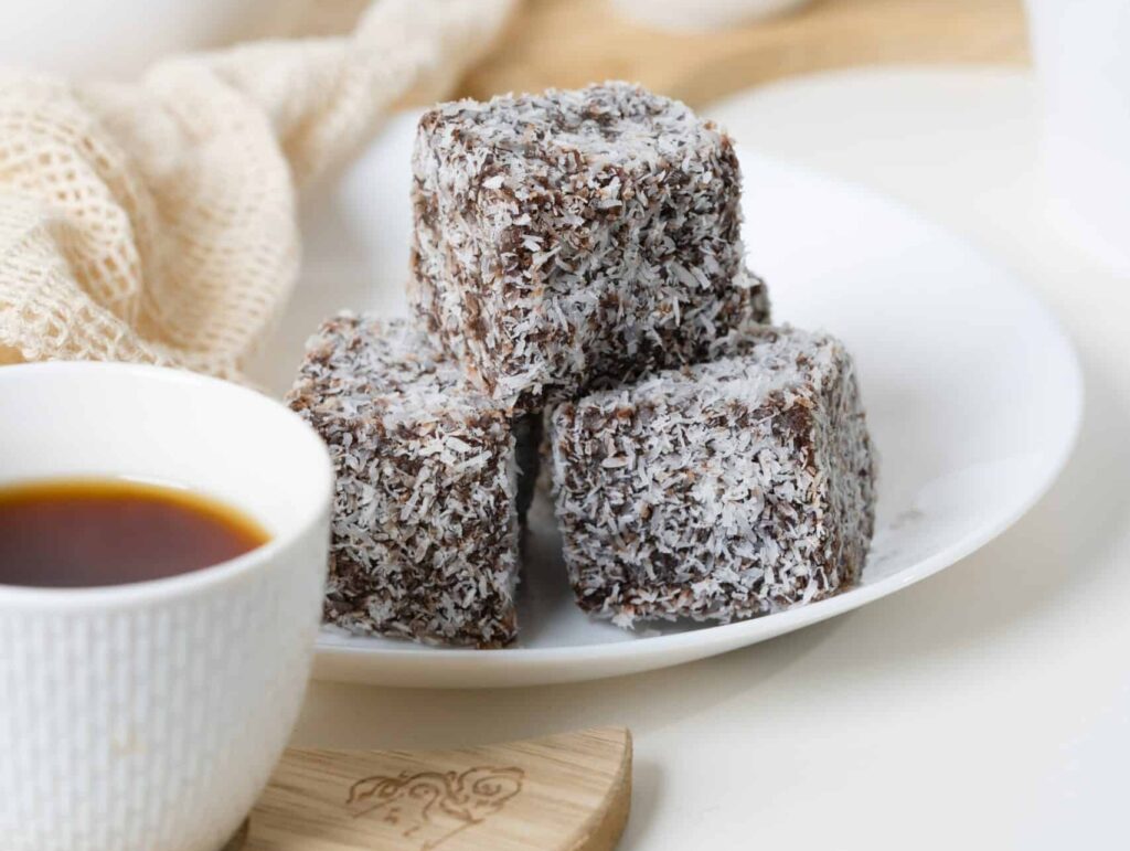 Australian food - A tray of lamington cakes sit on a white plate next to a cup of tea.