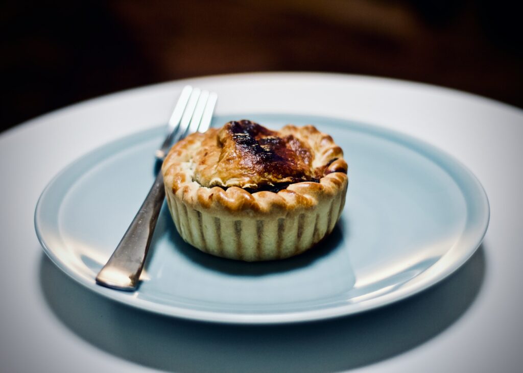 Australian food - an individually-sized meat pie sits on a blue plate with a fork.