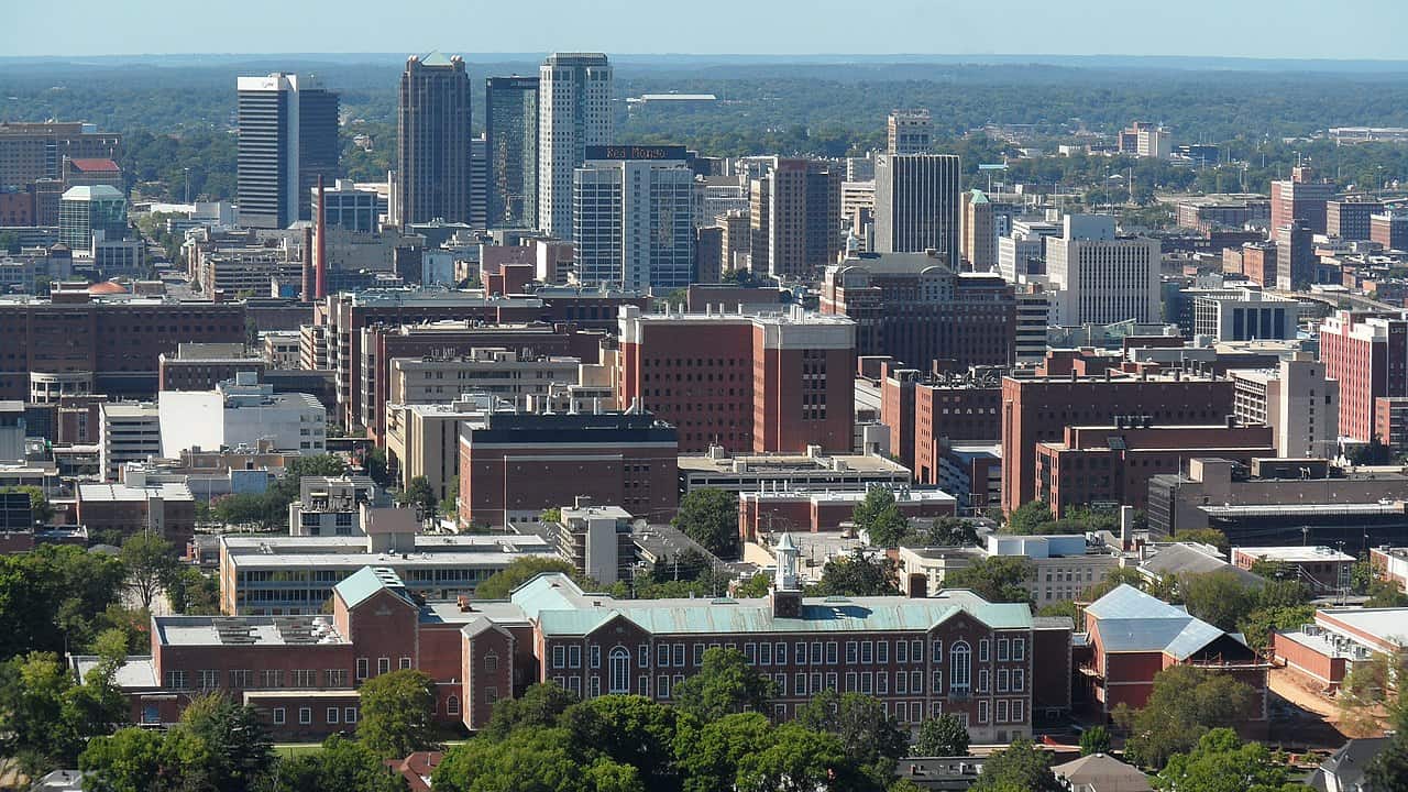 Birmingham, Alabama skyline: a mix of mid- and high-rise buildings, some brick, others steel and glass. Vulcan Park's trees are in the foreground.