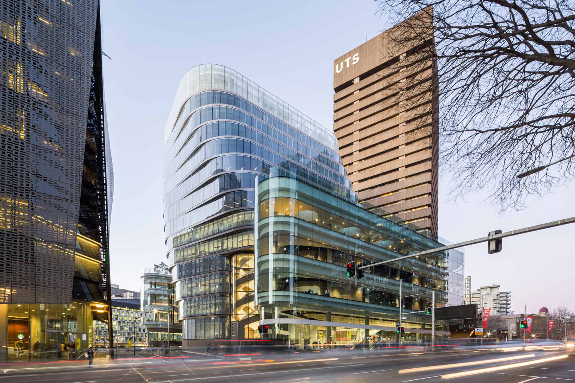 University of Technology Sydney's main building; a futuristic glass building with a slight upward curve on an urban street corner.