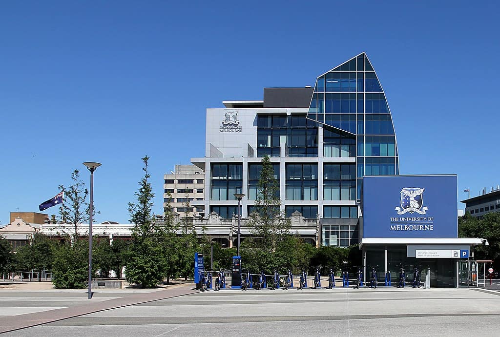 A university campus with modern steel and glass buildings. A row of bikes-for-rent are in the foreground, and an Australian flag is flying.