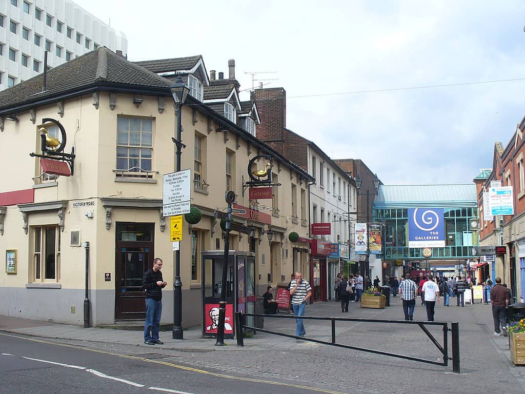 A pedestrian street in Aldershot, UK, with pubs, shops, and people walking.