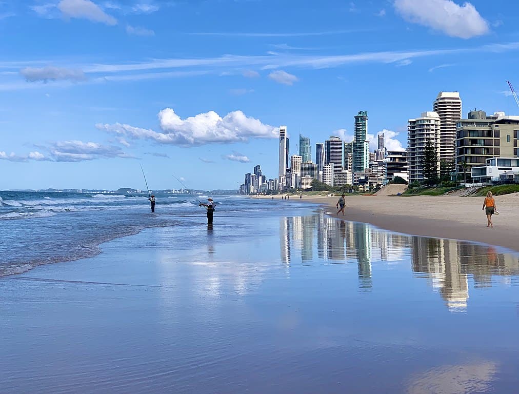 People fishing along a shallow beach, with a modern downtown behind them. (Queensland, AUS)