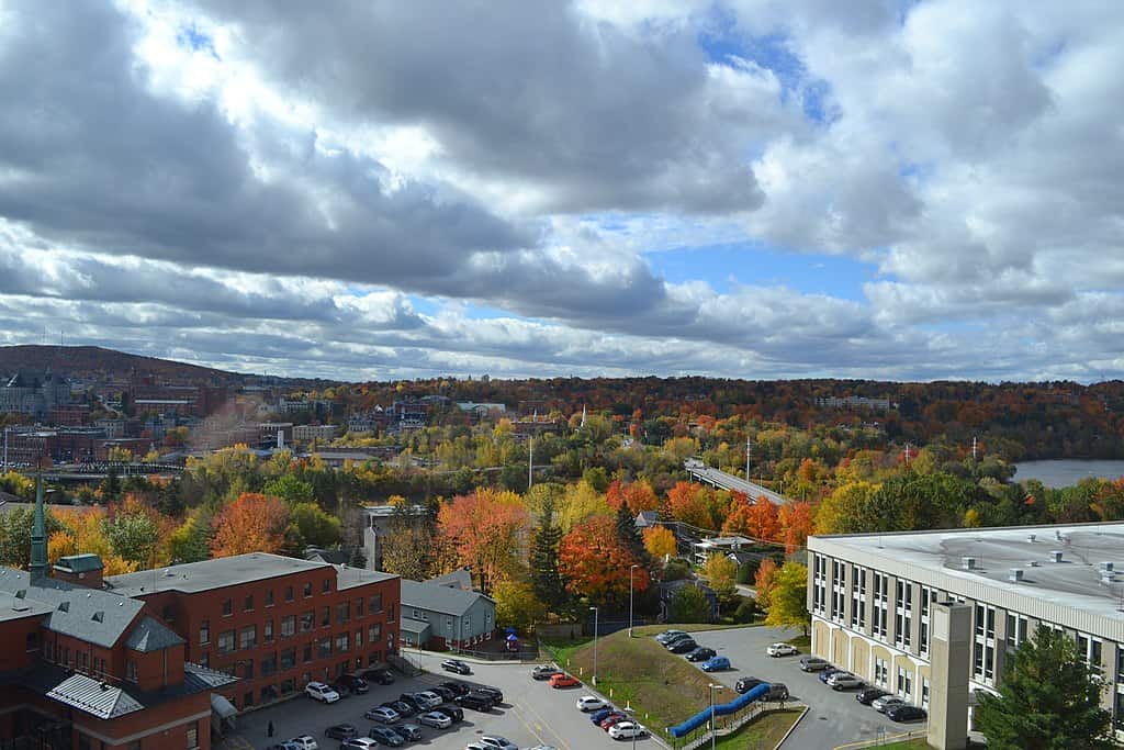 An autumn view of Sherbrooke, Quebec (brick buildings in the foreground, with a cityscape and rising hills behind.)