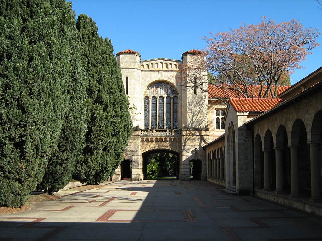 Winthrop Hall, UWA - a stone pathway leading to a building with high arches, lined by evergreen bushes.
