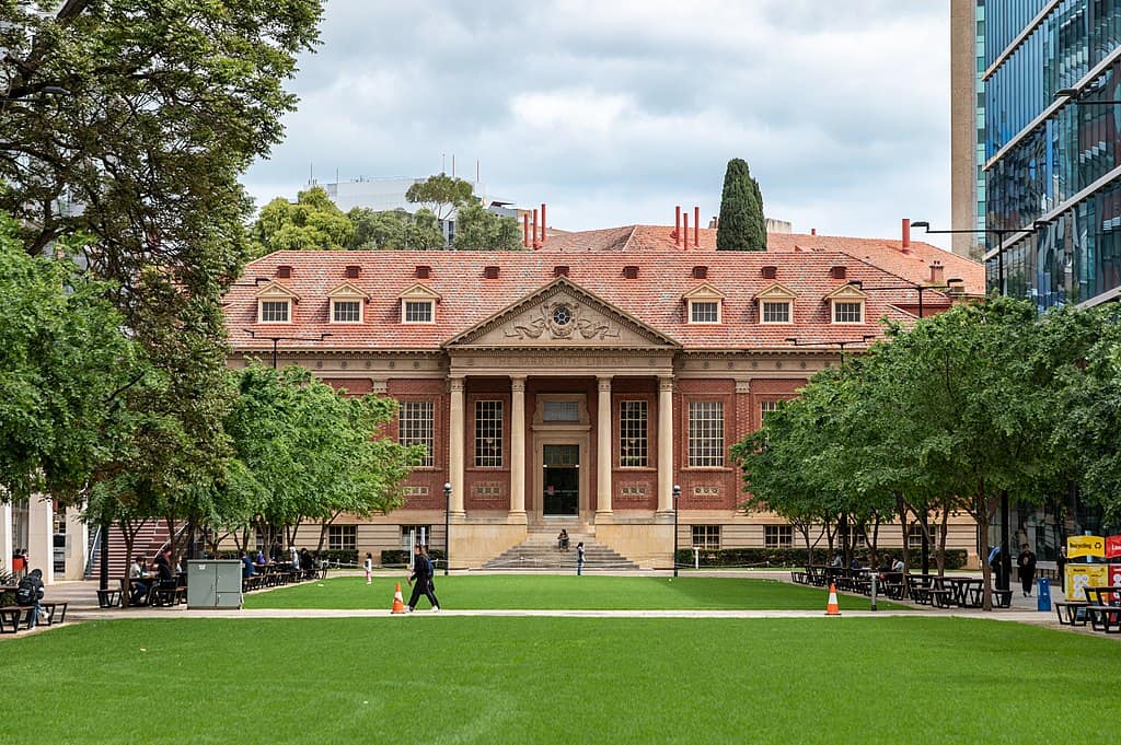 A red brick library adjacent to a large lawn, with people walking by (Barr Smith Library, University of Adelaide, Australia)