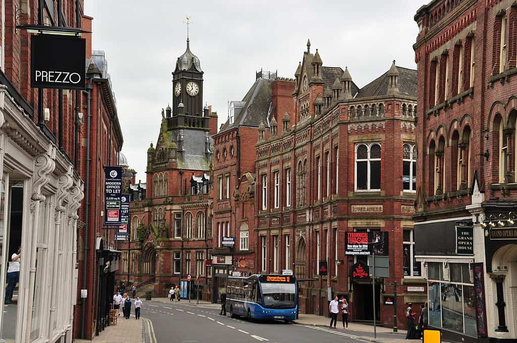 A city street with tall red-brick buildings and a blue city bus on the road. (York, UK)