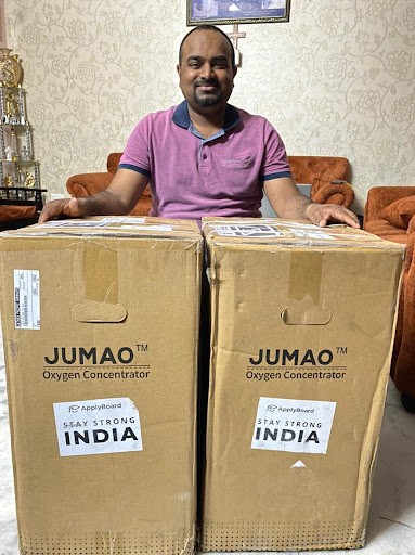 A photo of a man in front of two boxes of ventilators.