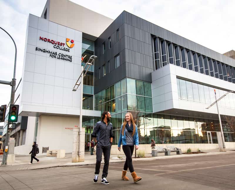 Two students walk in front of a large modern building (NorQuest College, Edmonton)