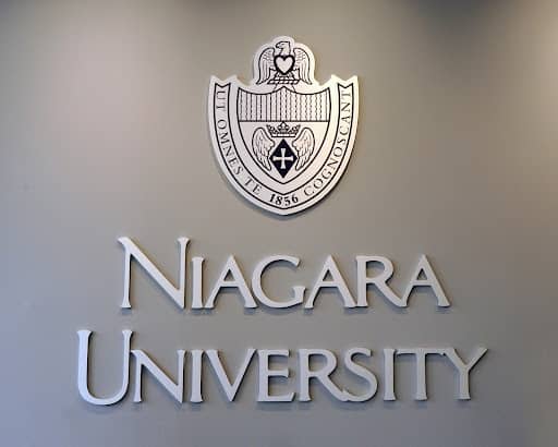 A grey wall, with the Niagara University name and official crest on it in silver and purple lettering.