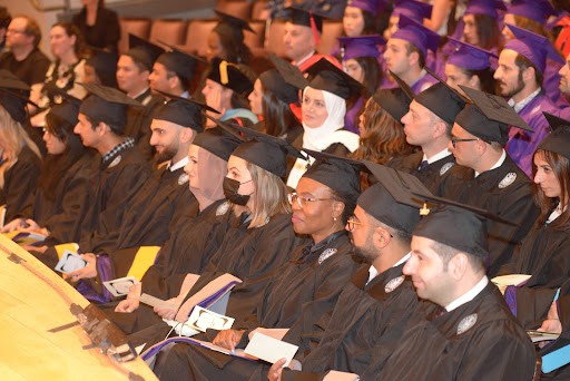 A group of students wearing graduation caps and gowns sit in lines.