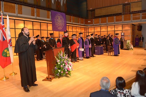 The stage at Niagara University in Ontario's graduation: an elevated stage built of warm-hued wood, with professors and ministry in ceremonial dress (lots of robes.)