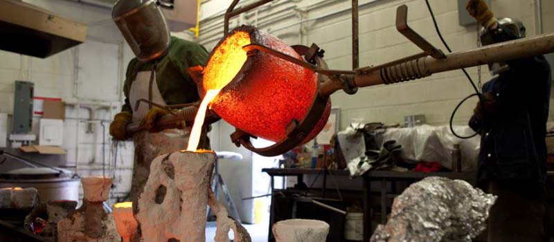 A student at OCAD University pours red-hot molten metal into a mold