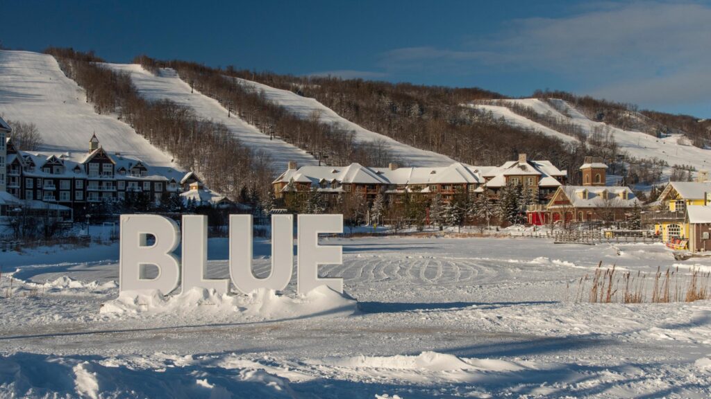 A photograph of The Blue Mountains resort in Canada with the words "Blue" on a sign outside the ski slopes.