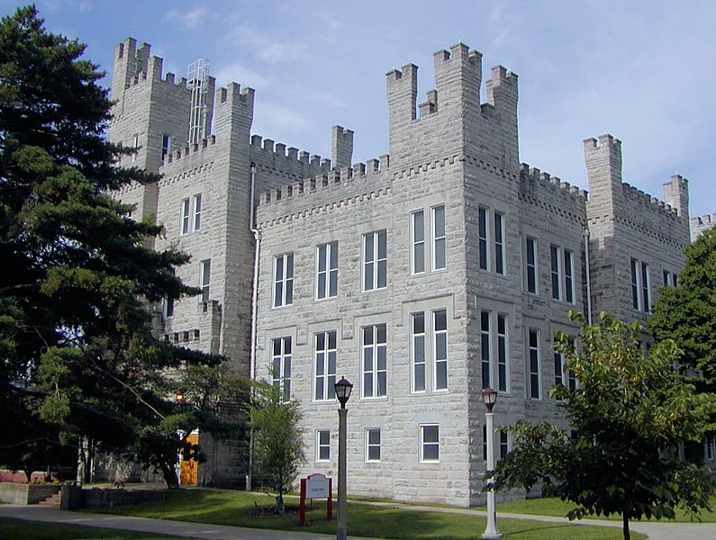 A grey brick castle-like building sits between groves of trees (Cook Hall, University of Illinois)
