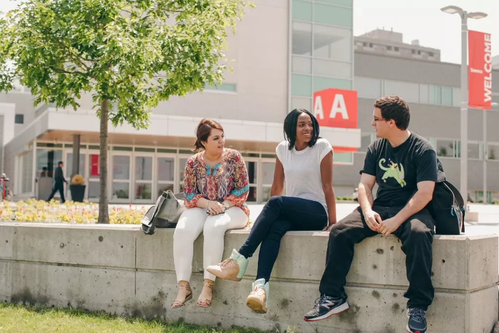 A photo of three students sitting outside on a sunny day at Seneca College Newnham Campus in Toronto.