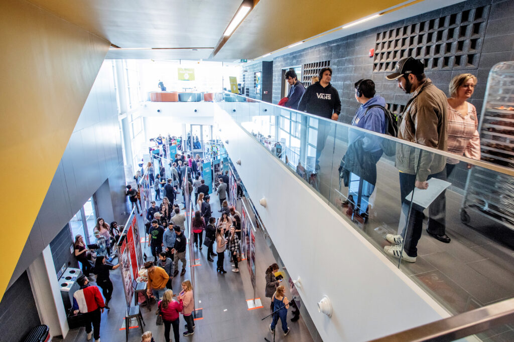 A busy campus hallway, looking down from the building's second storey. Students are walking around between classes.