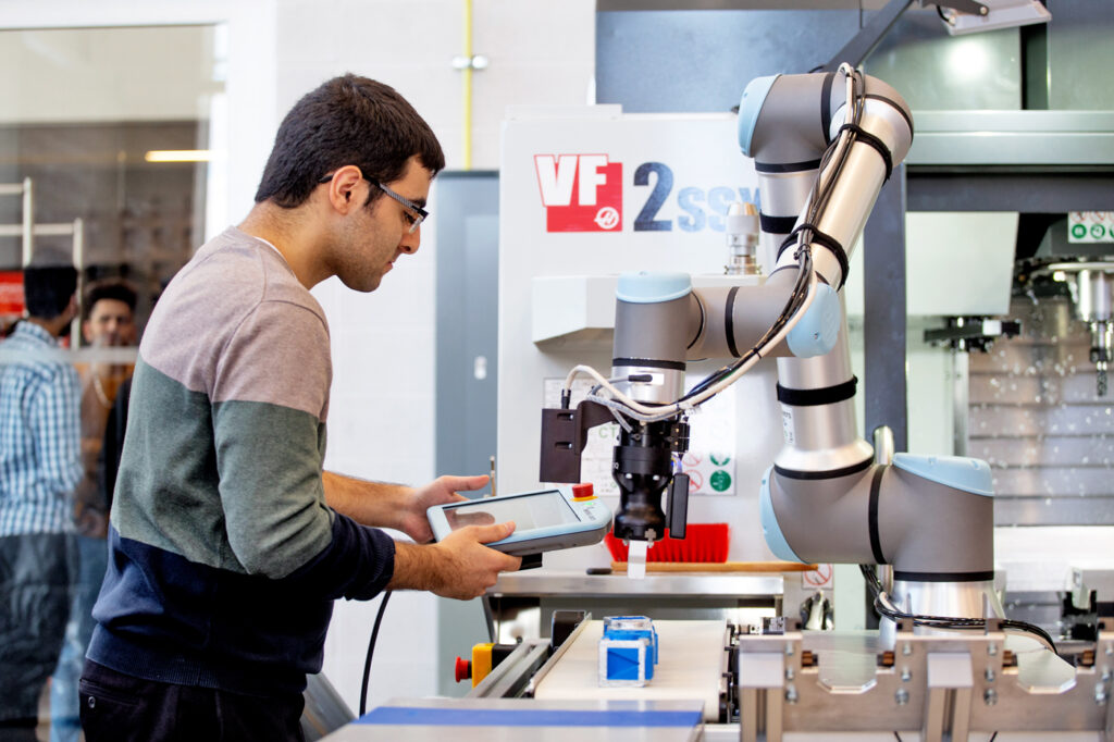 A young man works on a tech project with a machine that has a robotic arm.