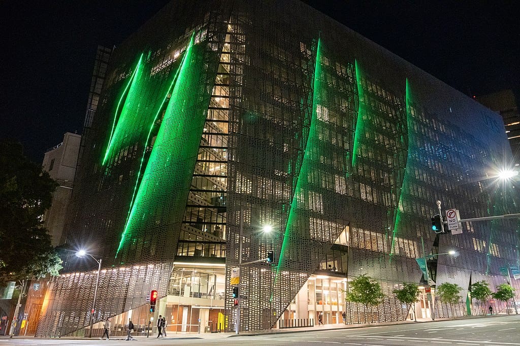 A multistorey, modern plate glass building, lit up by vertical green lighting, on a street corner in Sydney. (U of Tech Sydney)