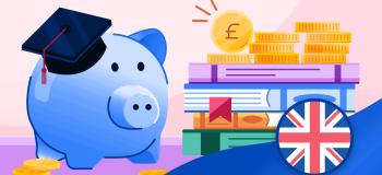 A blue piggy bank wearing a grad cap sits beside a stack of coins and books.